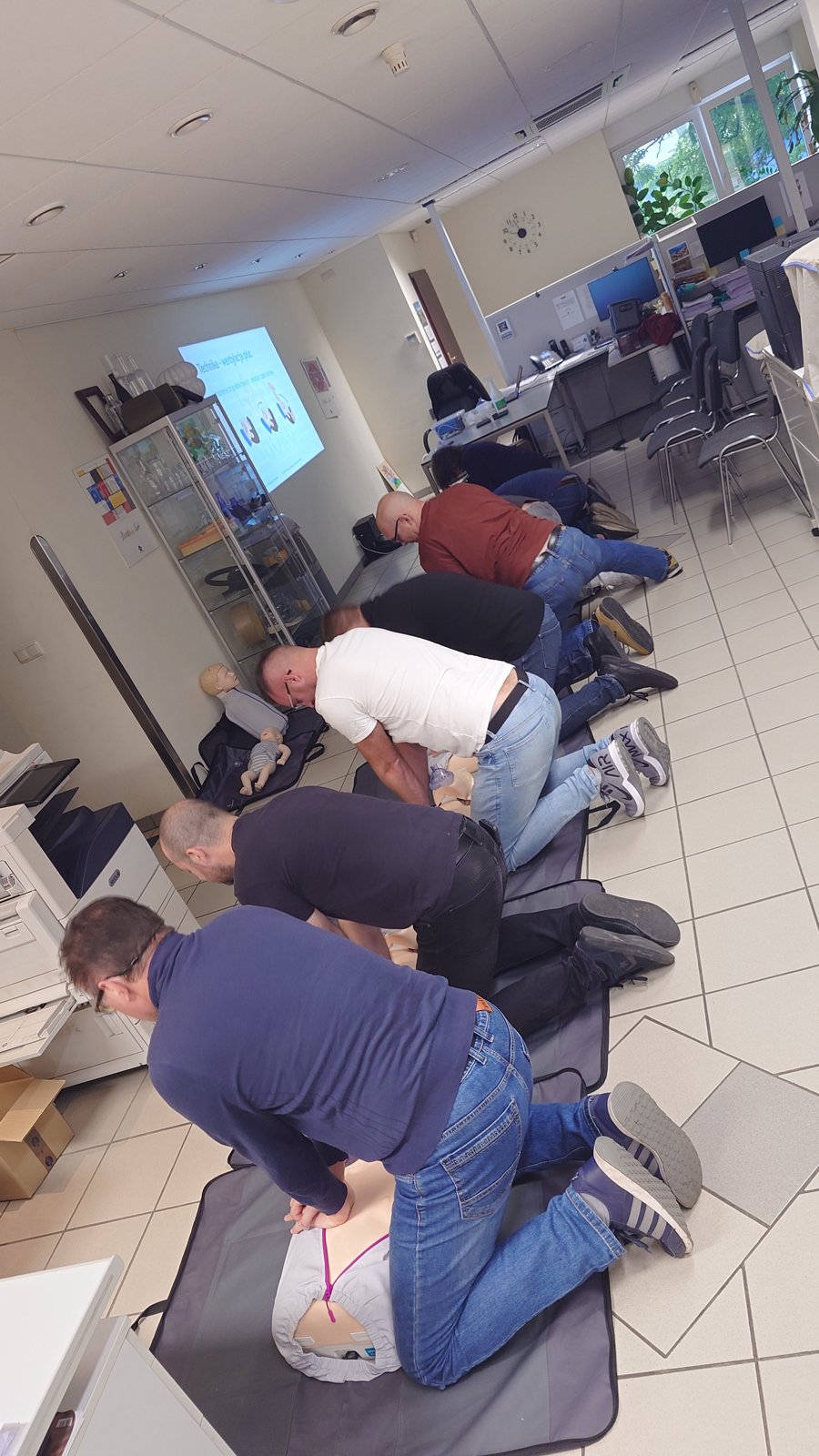 Uczestnicy szkolenia ćwiczą uciskanie klatki piersiowej w biurze