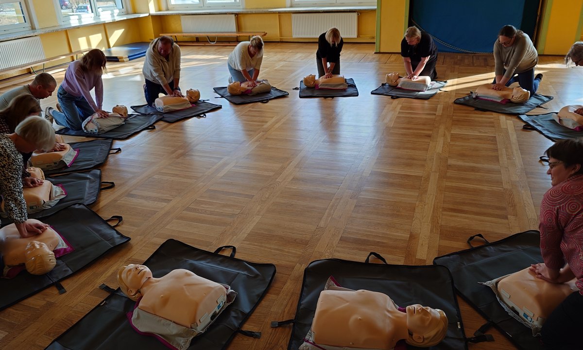 Grupa uczestników ćwiczy resuscytację na manekinach ustawionych w kręgu